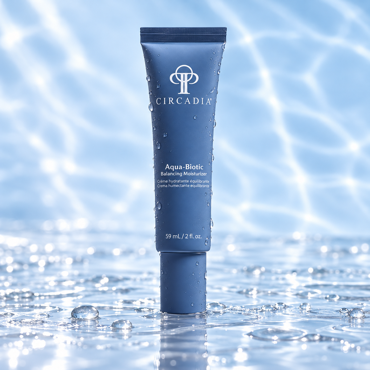 A tube of Circadia Aqua-Biotic Balancing Moisturizer stands upright in shallow water, with droplets on the tube and a bright blue water-ripple background.