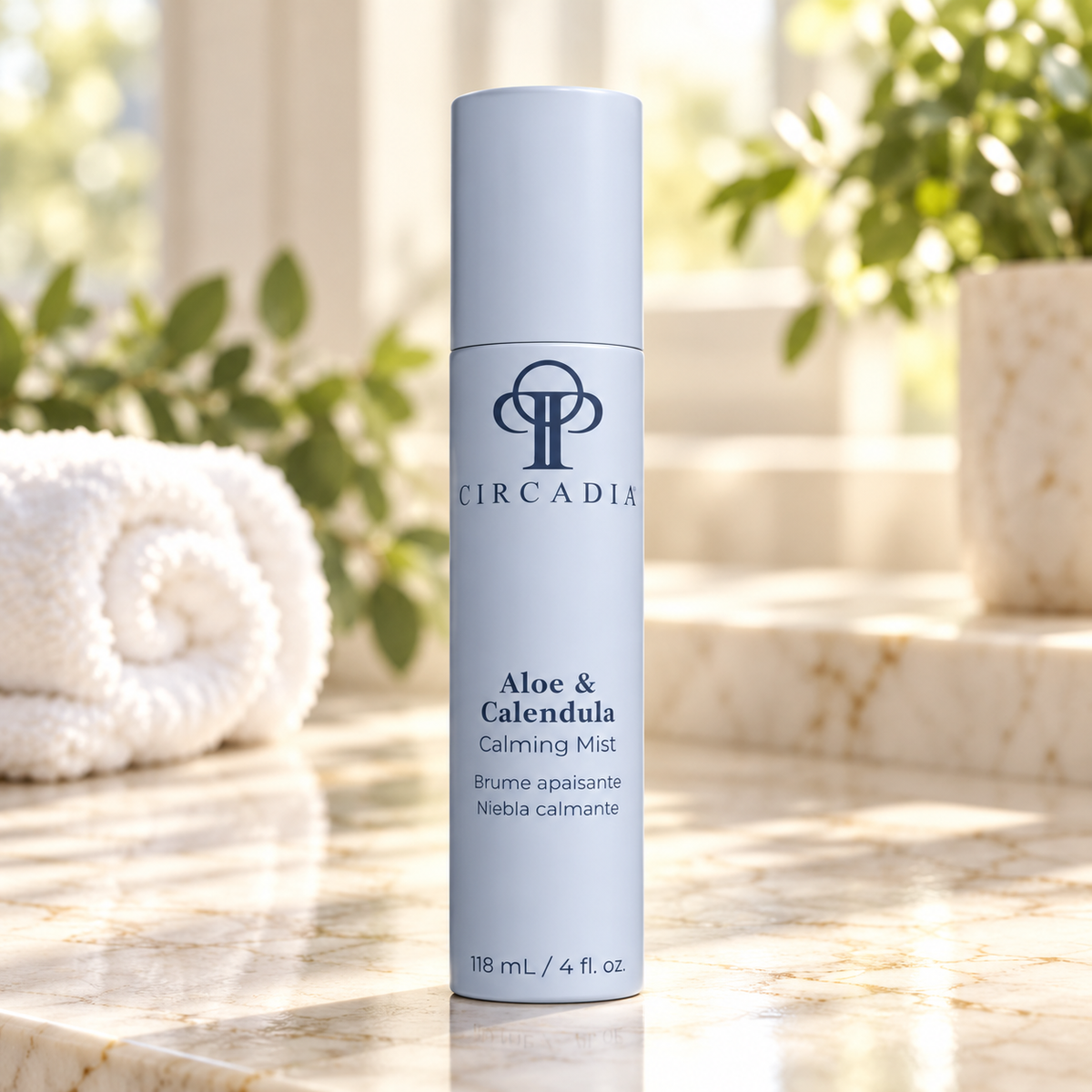 A cylindrical bottle of Circadia Aloe & Calendula Calming Mist stands on a marble surface with a rolled towel and green plants softly blurred in the background.