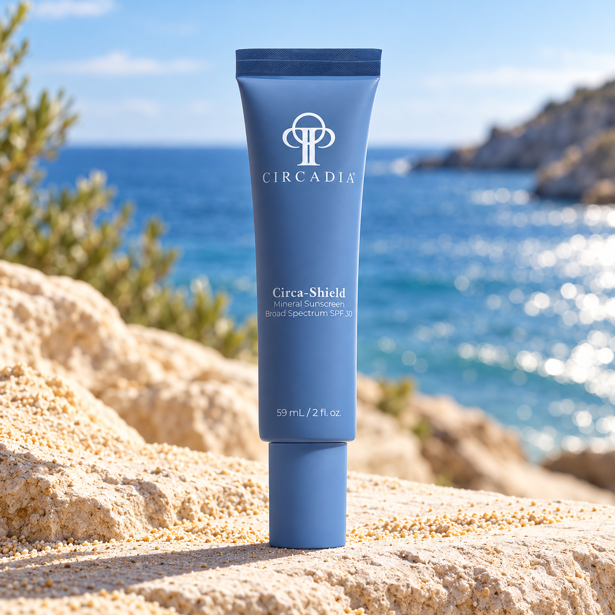 A blue tube of Circadia Circa-Shield Natural Conditioner standing upright on a sandy beach with the ocean in the background.