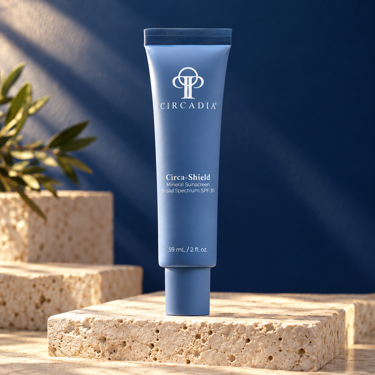 A tube of Circadia Circa-Shield Broad Spectrum SPF 30 sunscreen stands upright on a textured stone pedestal against a dark blue background with soft sunlight and shadow patterns.