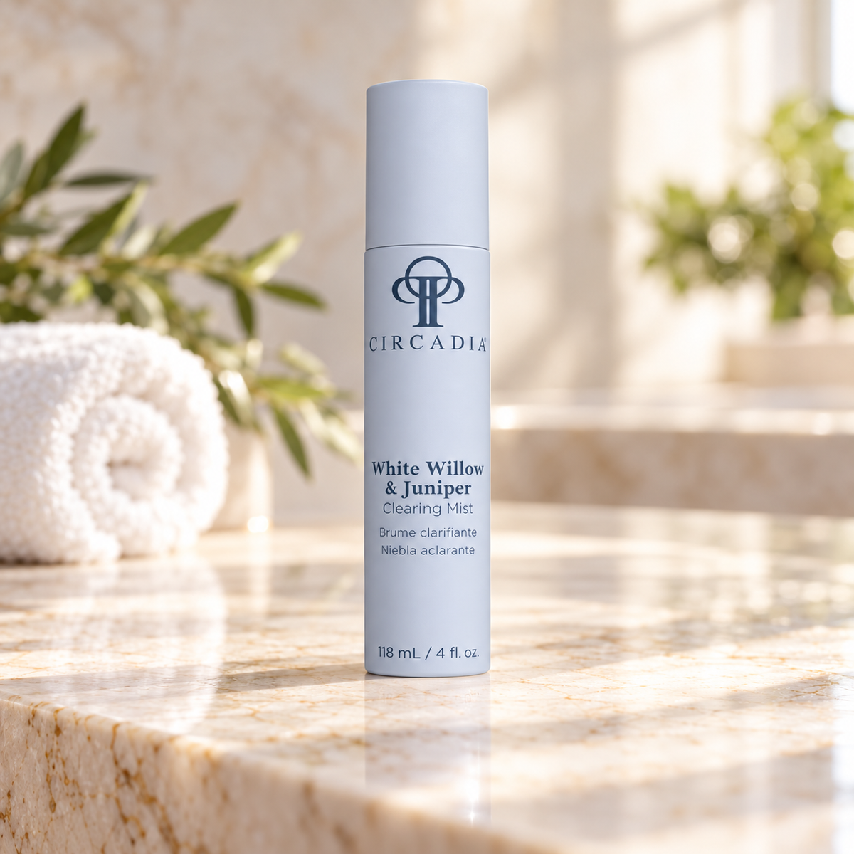 A cylindrical bottle of Circadia White Willow & Juniper Clearing Mist stands on a polished stone countertop in a bright bathroom setting, with a rolled towel and soft-focus greenery in the background.