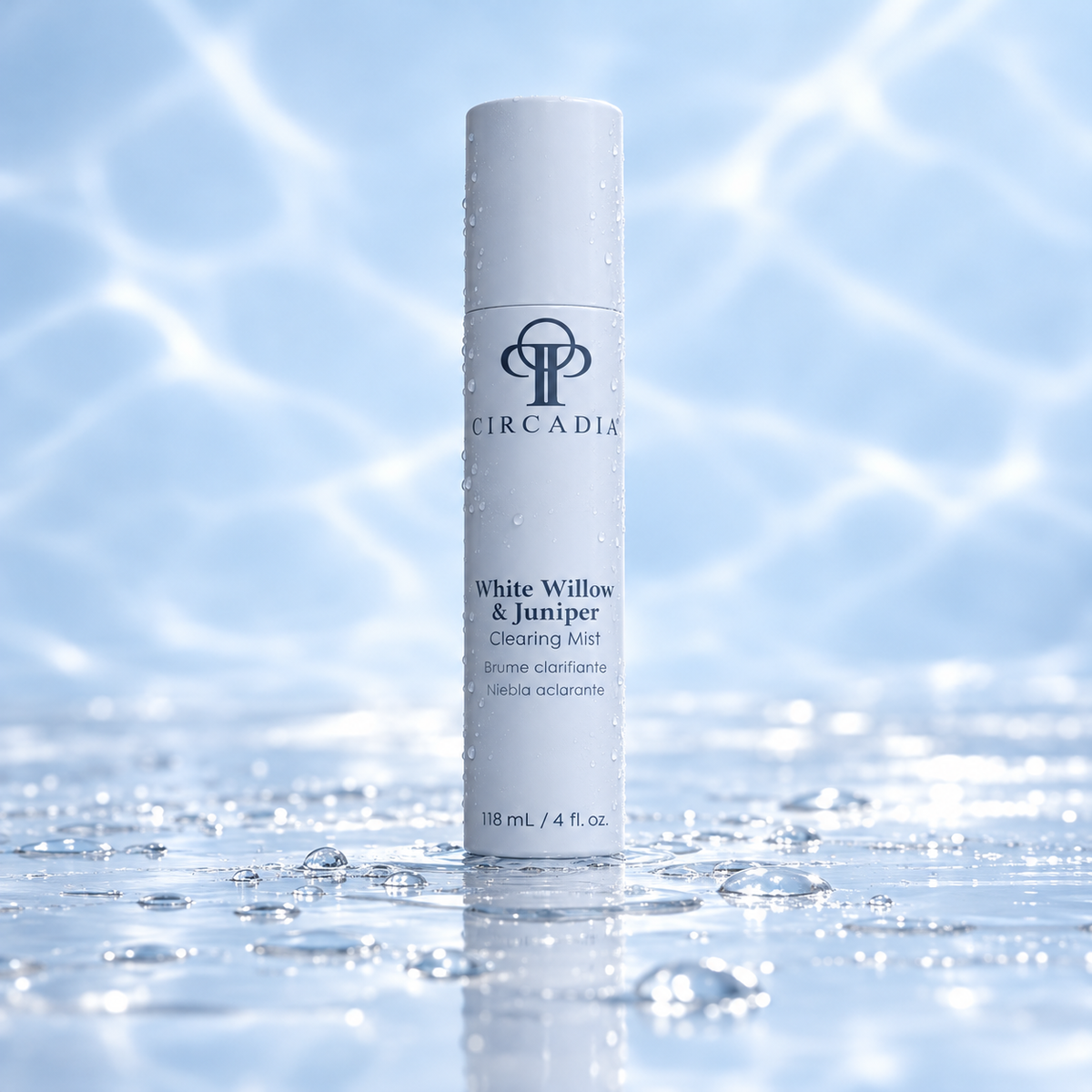 A white cylindrical bottle of Circadia White Willow & Juniper Clearing Mist stands upright in shallow water with ripples and droplets on the bottle, against a soft blue background with light reflections.