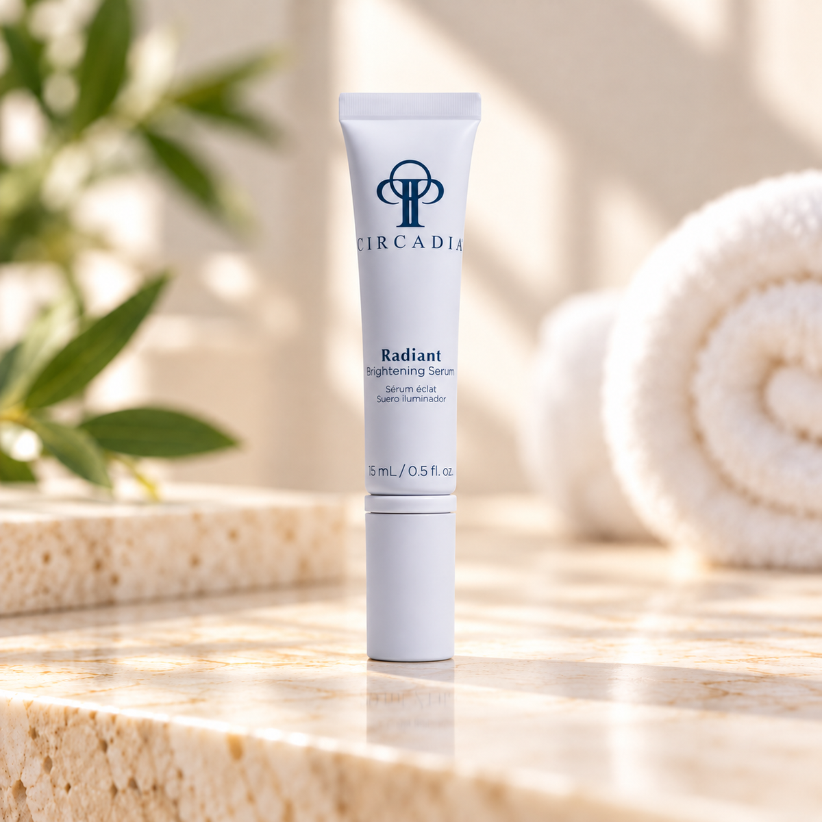 A 15ml white tube of Circadia Radiant Brightening Serum stands on a beige stone surface with a blurred spa-like background featuring green leaves and a rolled white towel.