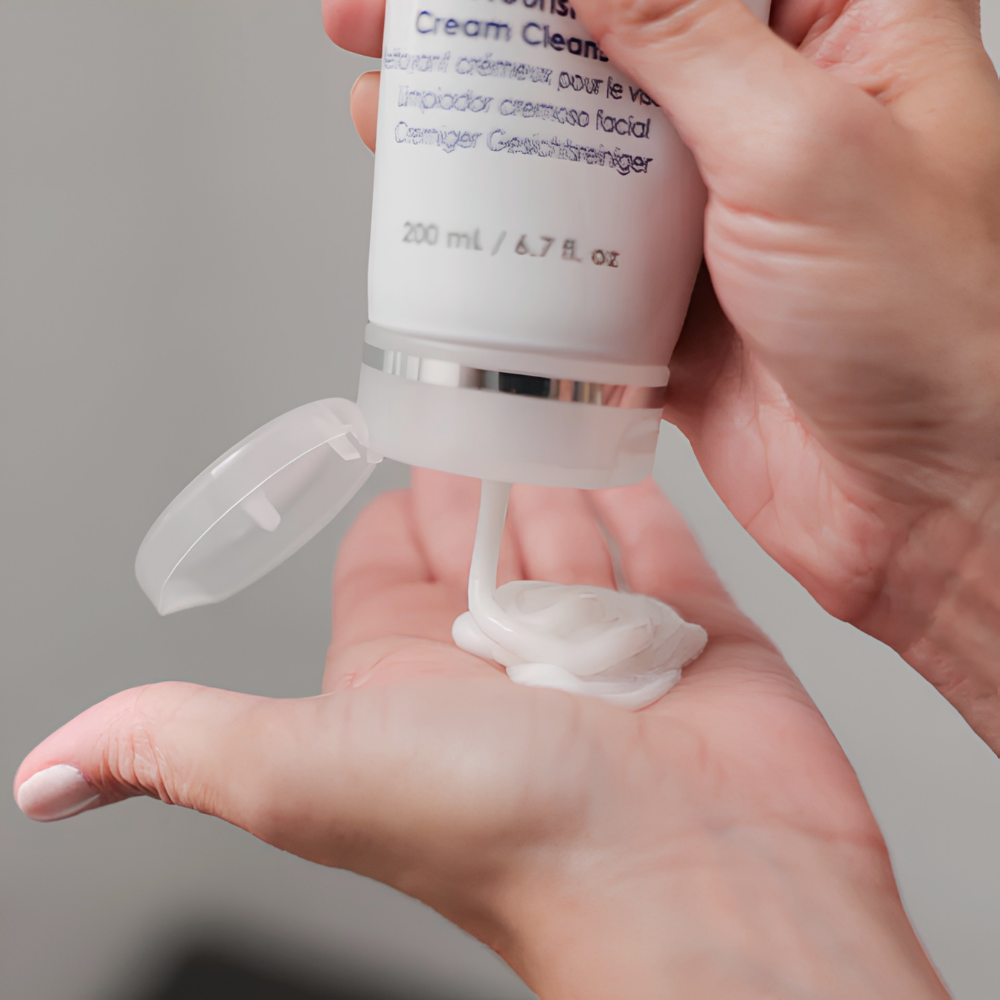 Person holding a skincare product with cream being dispensed onto the palm.